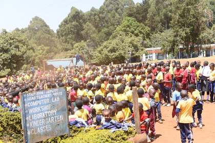 A crowd of learners beside a directional signboard listing school facilities.