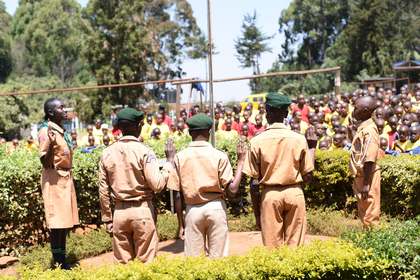 Scouts in uniform saluting at the flagpole during assembly.
