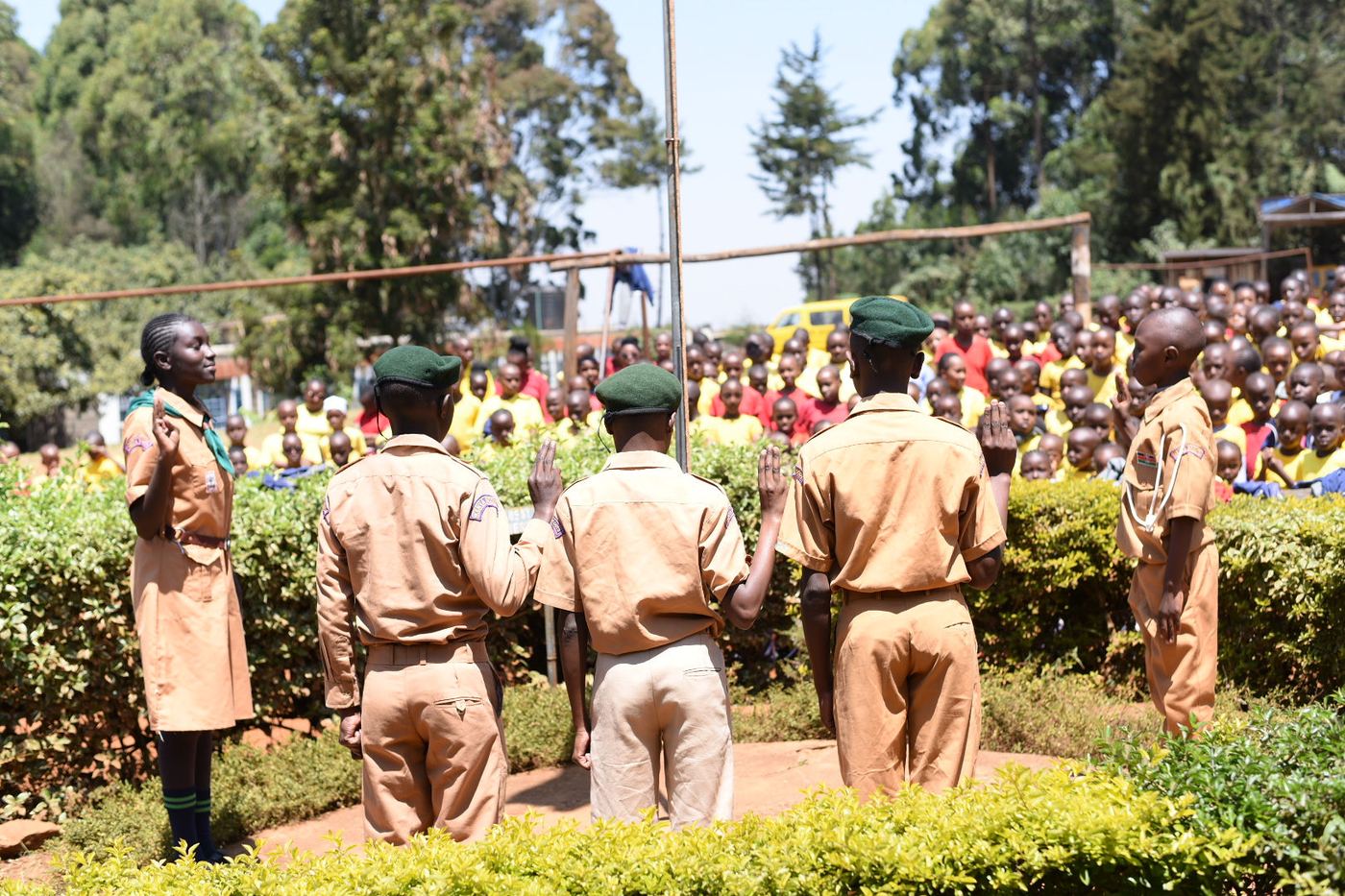 Scouts in uniform saluting at the flagpole, with the whole school assembled behind them.